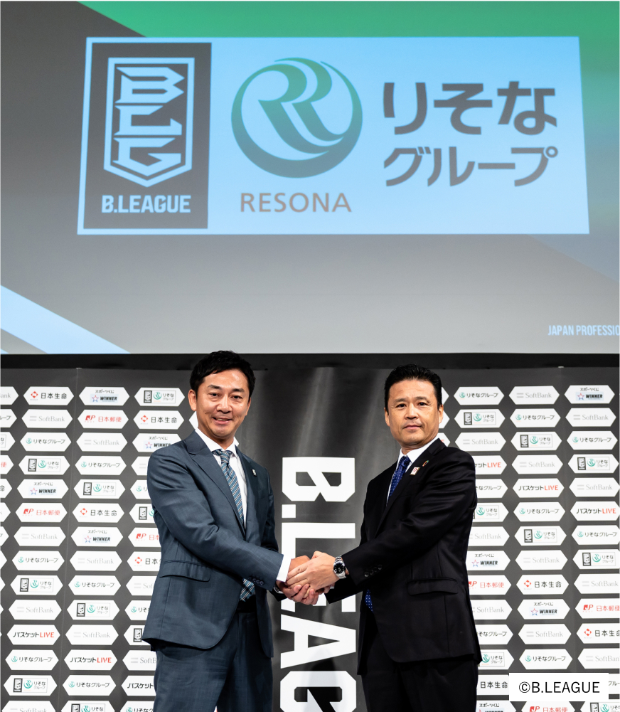 Bリーグとりそなグループのロゴの下で島田チェアマンと南社長が両手で握手をしいている写真