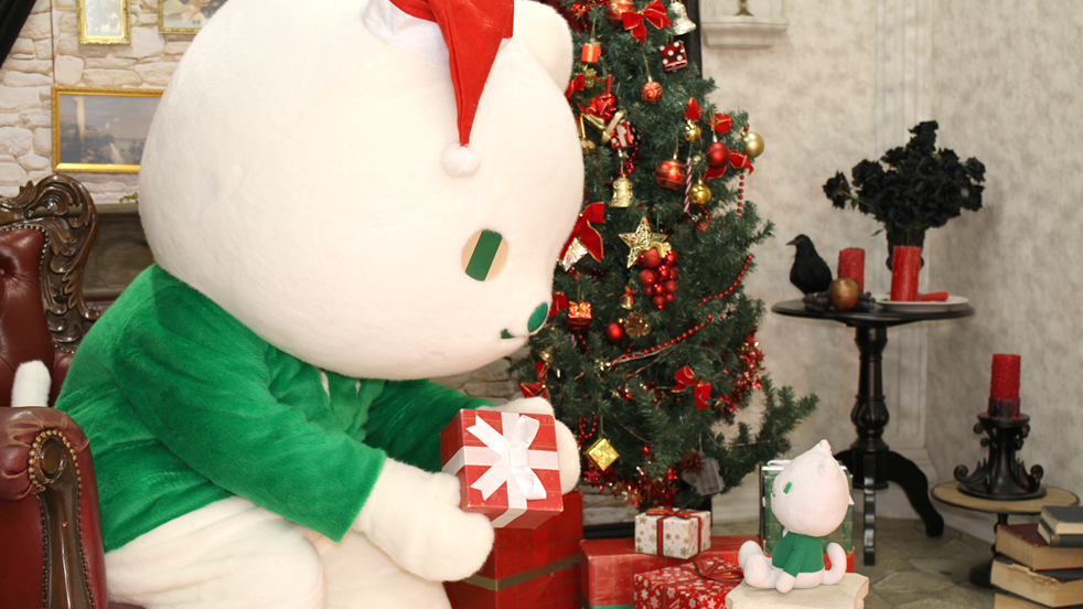 ツリーの前でりそにゃがぬいぐるみを相手にクリスマスプレゼントを渡す練習をしている画像